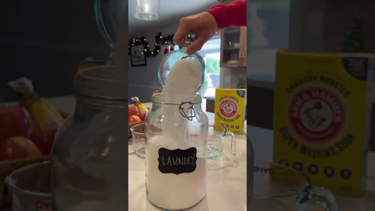 A person pours white powder from a measuring cup into a jar labeled "Laundry" next to a box of Arm & Hammer Super Washing Soda in a kitchen setting.